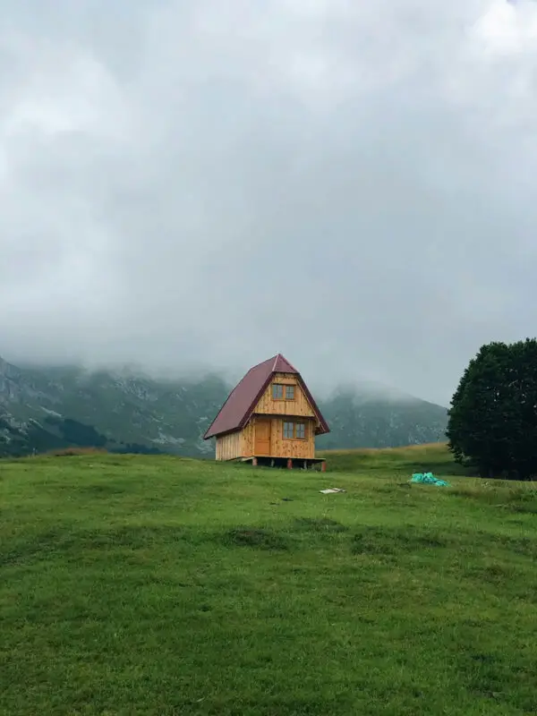 Cabane en bois isolée sur une prairie verdoyante dans les montagnes du Jura, sous un ciel nuageux