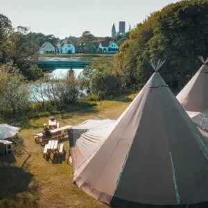 Tipi en face d'une rivière, entouré d'arbres et de verdure .