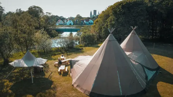 Tipi en face d'une rivière, entouré d'arbres et de verdure .